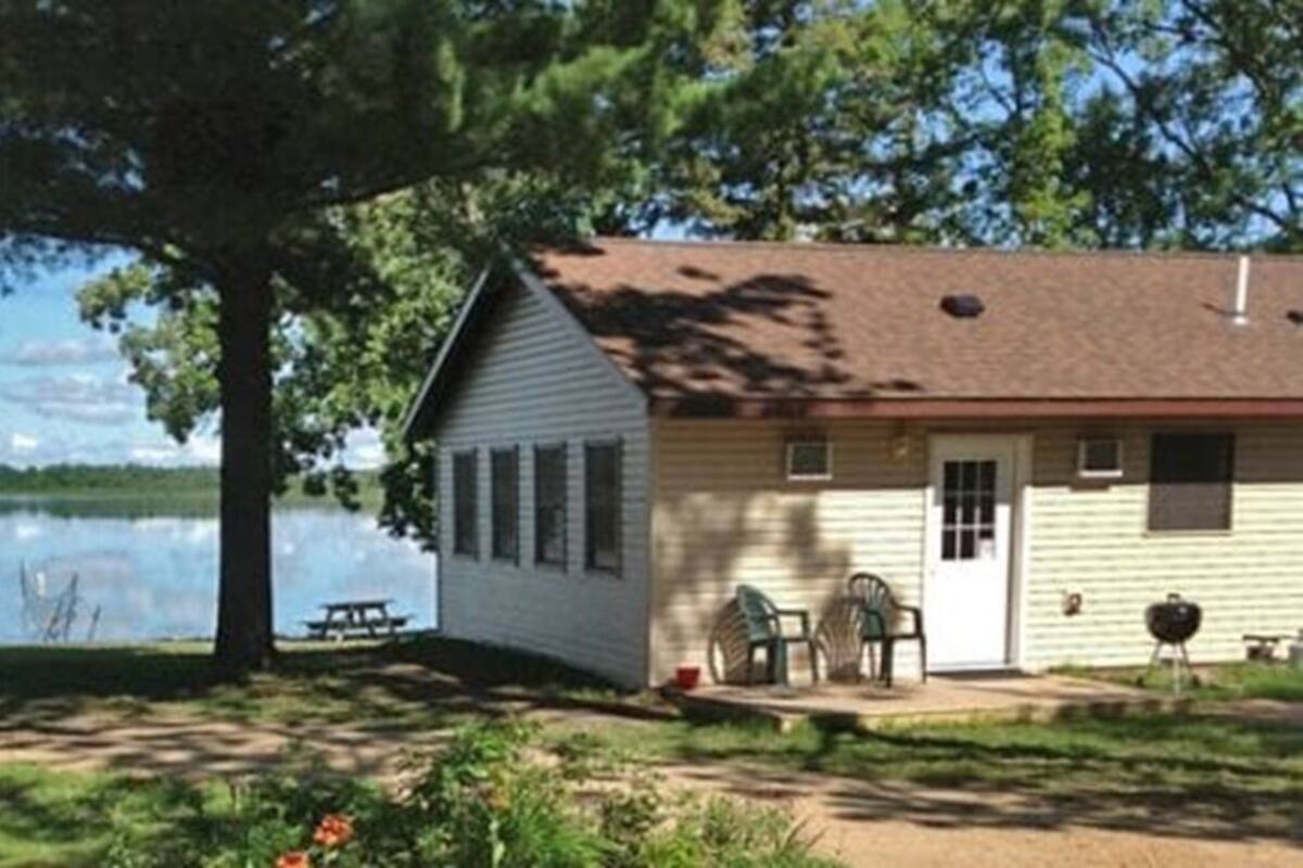 Une petite cabane avec un quai, une table de pique-nique et un barbecue, située près d’un lac.