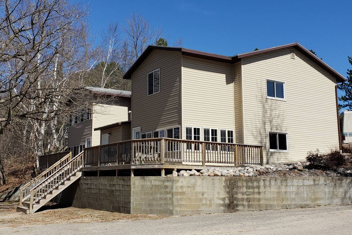 Une maison à deux étages dotée d’une terrasse en bois et d’un mur de soutènement en pierre.