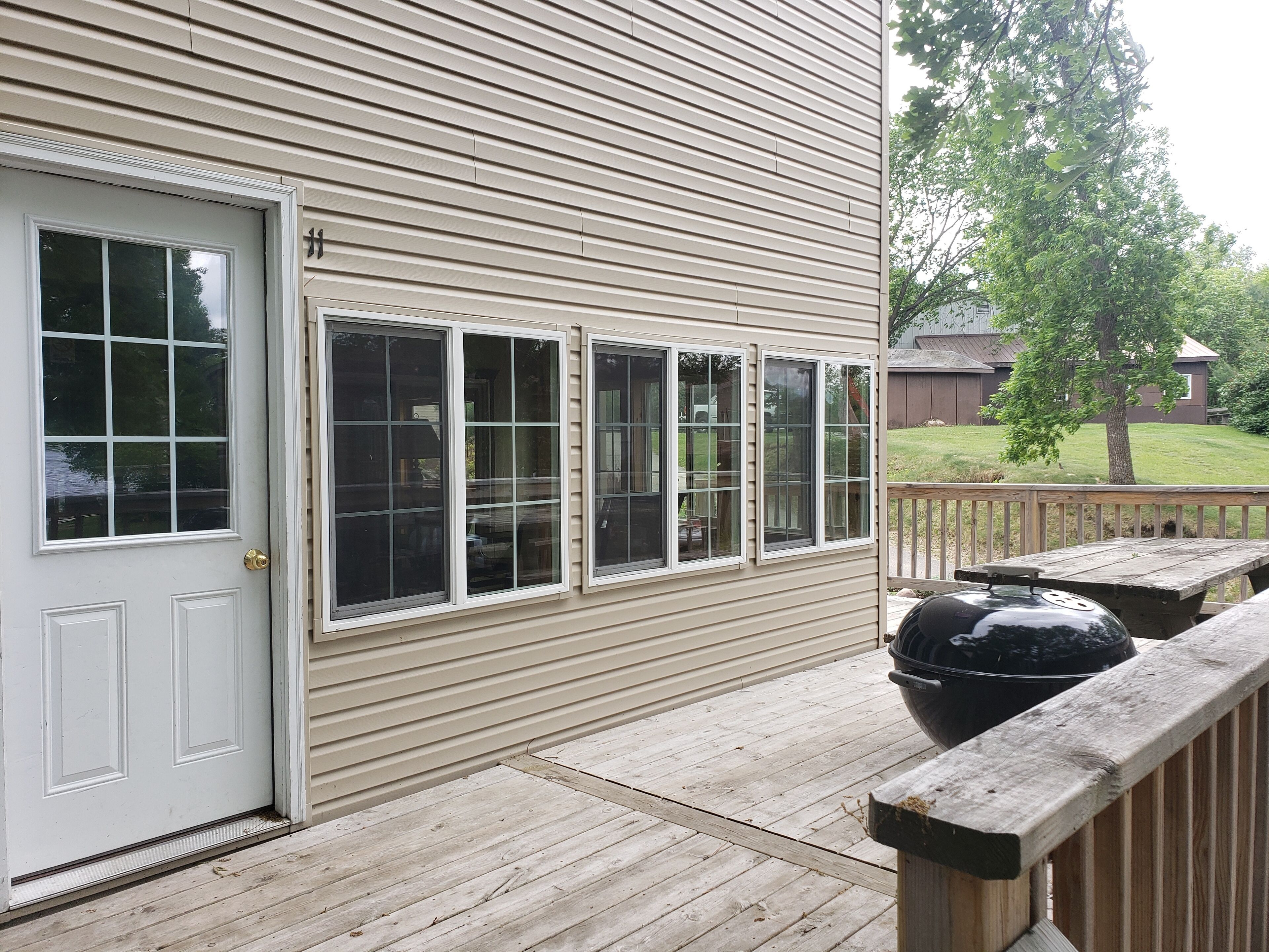 A house with a front door, three windows, a wooden deck, and a barbecue grill.