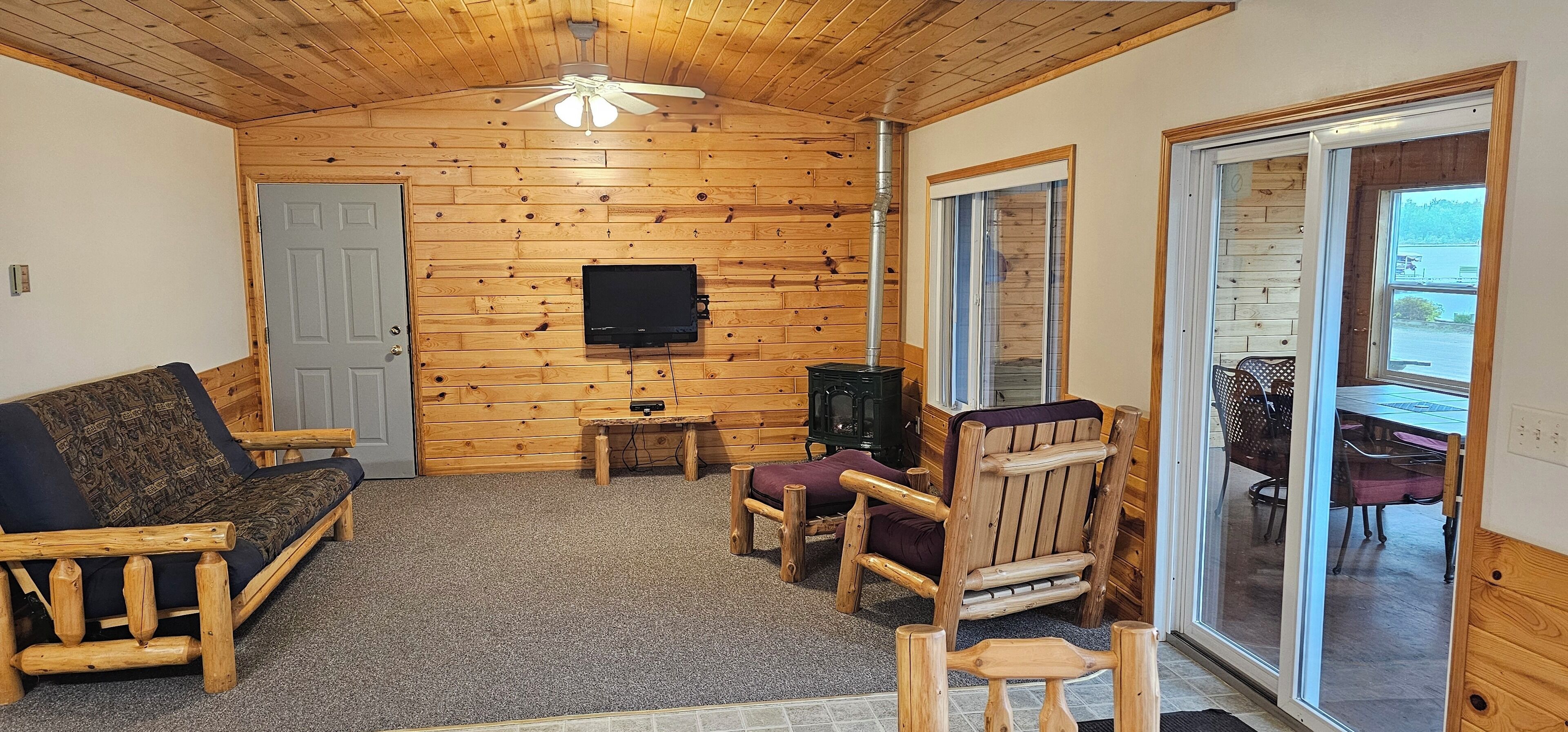 Interior acogedor de una cabaña con techo de madera, televisor, chimenea y puerta corrediza de vidrio que da a un espacio exterior.