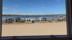 Vista desde una ventana con vista a un puerto deportivo con barcos amarrados y una playa arenosa al frente.