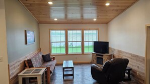 Una sala de estar acogedora con techo de madera, un sofá, un sillón reclinable, una mesa de centro y un televisor sobre un soporte de madera.
