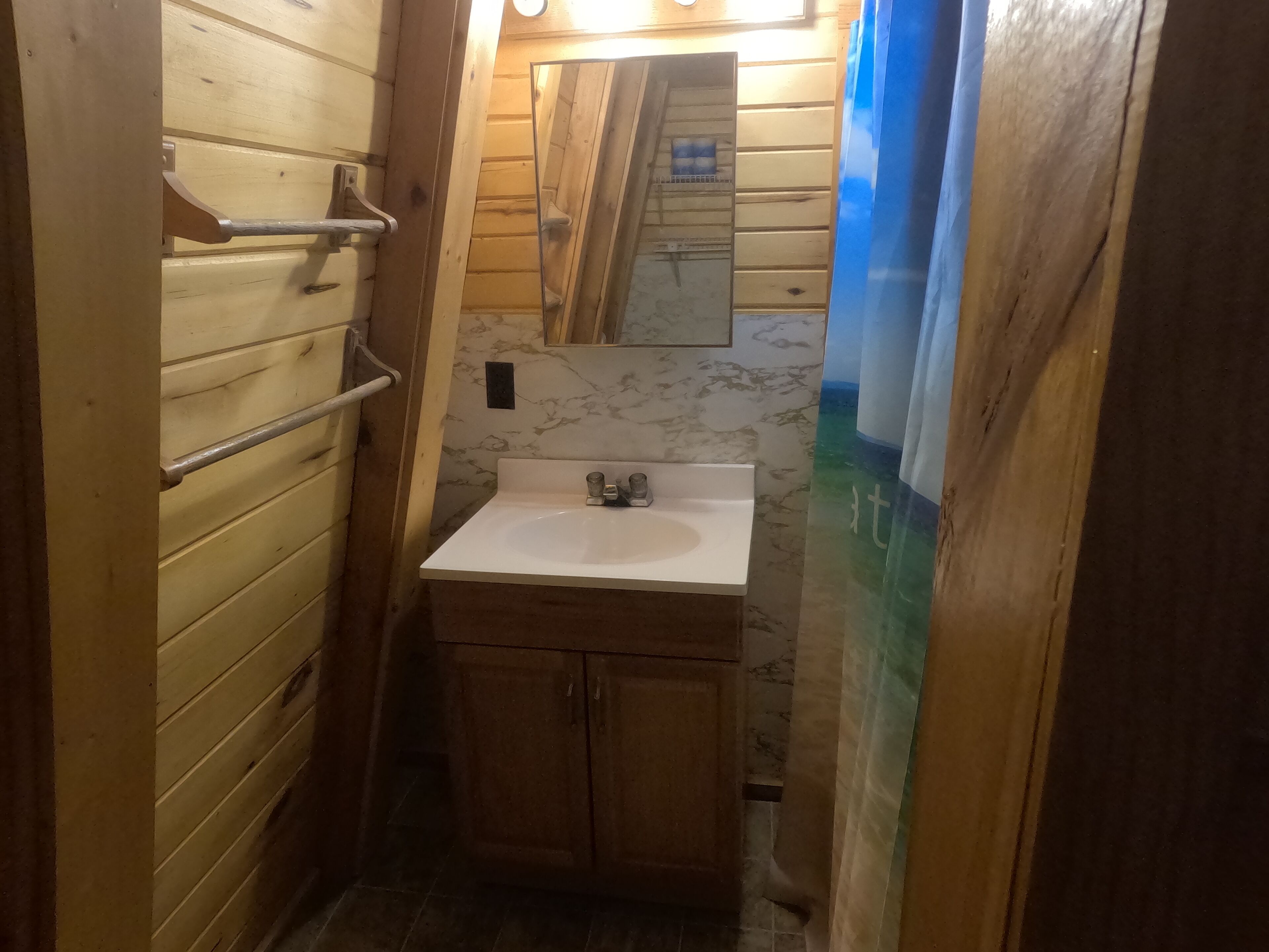 Ein schmales Badezimmer mit Holzwänden, einem weißen Waschbecken und einem Spiegel darüber.