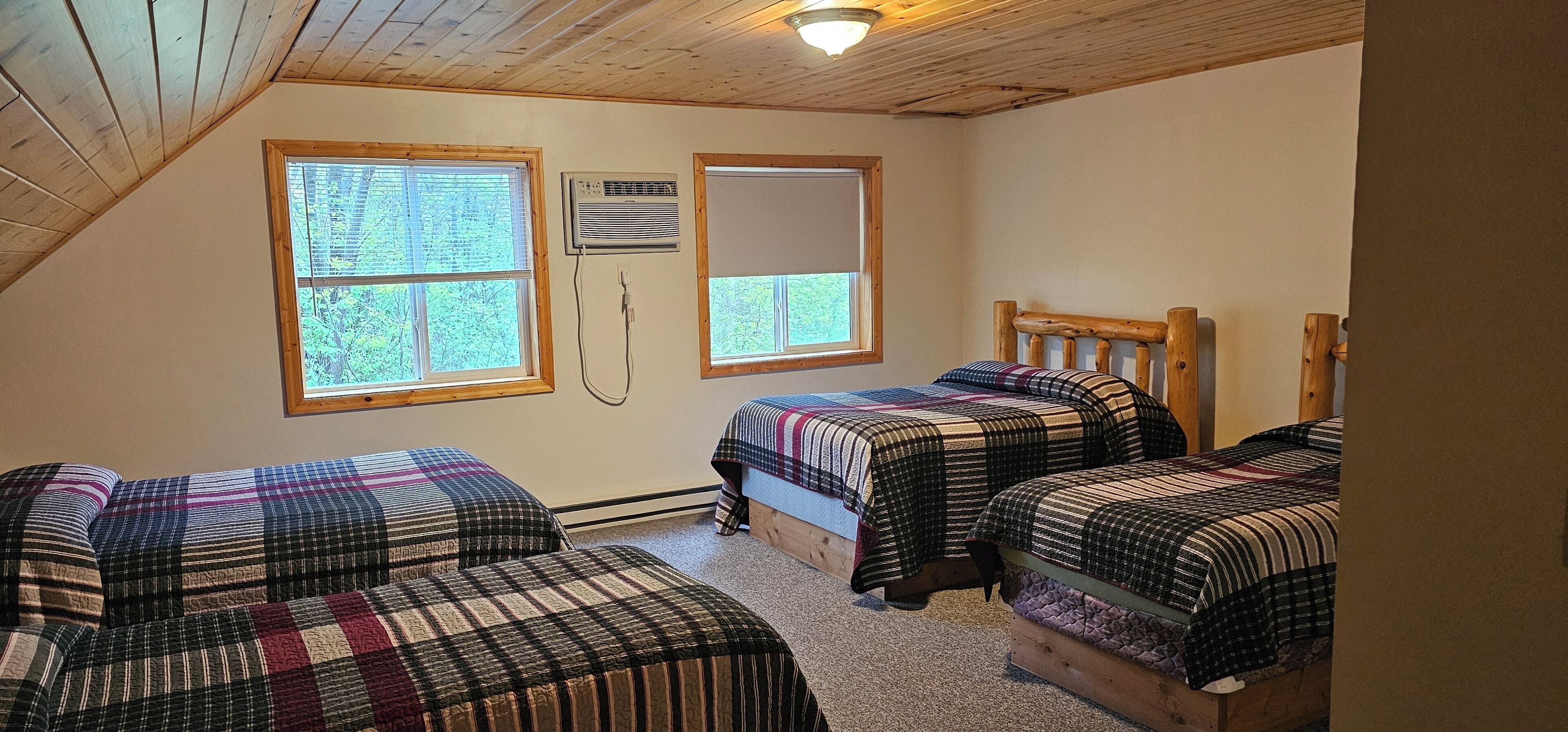 A bedroom with two beds, wooden headboards, and large windows with blinds.