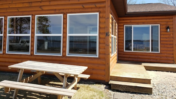 Una cabaña de madera con ventanas amplias, una mesa de picnic y una terraza.