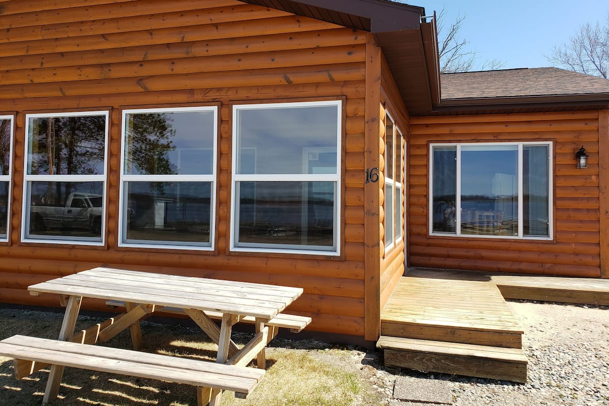 Une cabane en bois dotée de grandes fenêtres, d’une table de pique-nique et d’une terrasse.