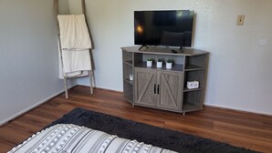 Ein Schlafzimmer mit einem Bett, einem Fernseher auf einer Holzkommode, einem flauschigen Teppich und einem Holzstuhl mit weißem Handtuch.