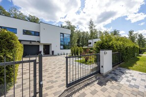 Una casa moderna de dos pisos con entrada por un camino pavimentado y puerta de acceso cerrada.