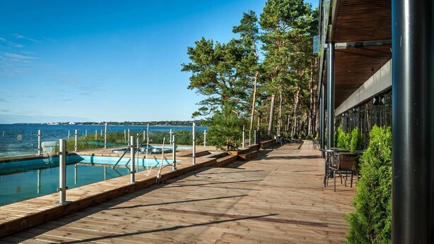 Una terraza de madera con piscina, con vista a un cuerpo de agua y una costa lejana.