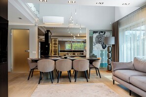Un comedor moderno con una mesa central y sillas, un sofá, y un ventanal con cortinas.