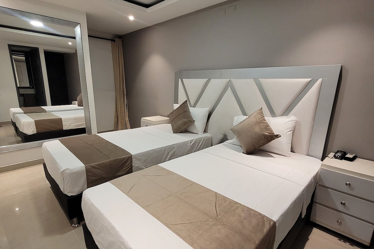 A modern hotel room with two beds, a large mirror, and a nightstand with a phone.