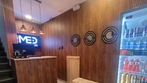 A reception area with a wooden wall, a reception desk, a bench, a refrigerator stocked with beverages, and a staircase. - Hotel Med 33 (Medellín)