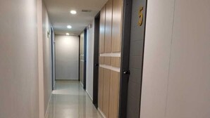 A long, narrow hallway with a shiny tiled floor, wooden doors, and a number 5 on one door. - Hotel Med 33 (Medellín)