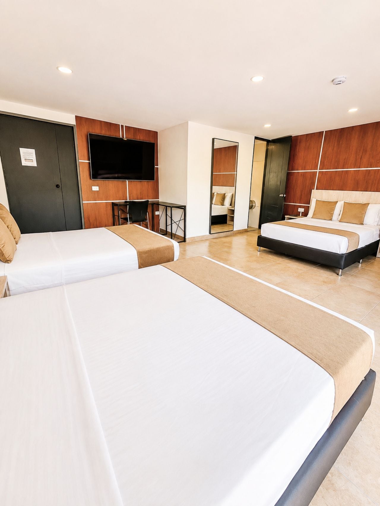Habitación de hotel con dos camas, televisión, escritorio y espejo.
