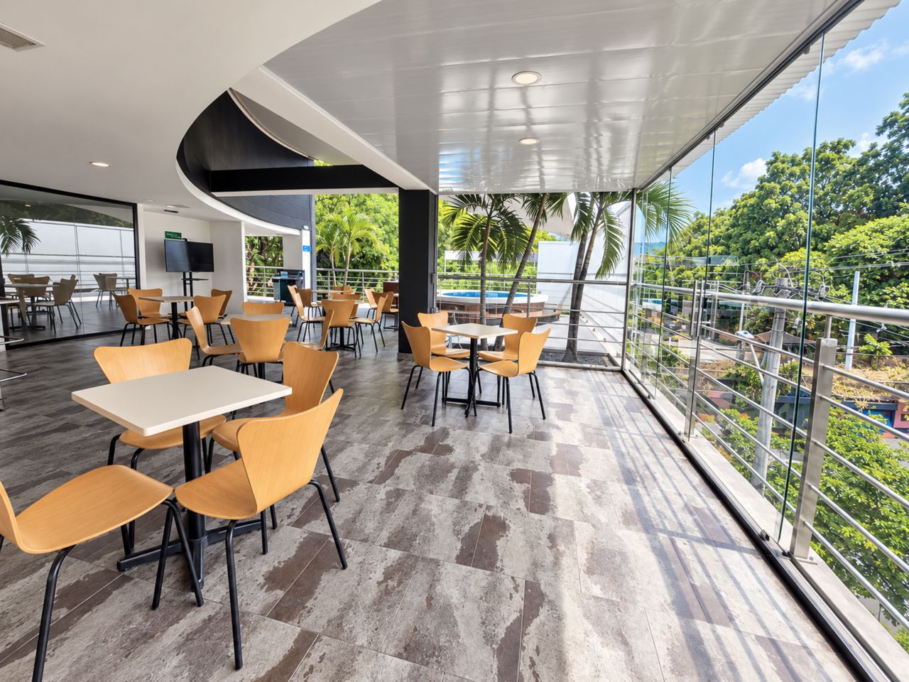 A modern outdoor seating area with tables and chairs, large windows, and a view of greenery.