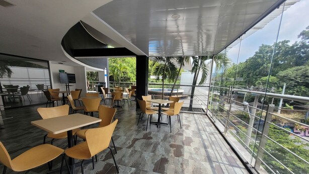 A spacious outdoor cafe with modern furniture and large windows offering a view of the surrounding greenery. - Hotel Med 33 (Medellín)