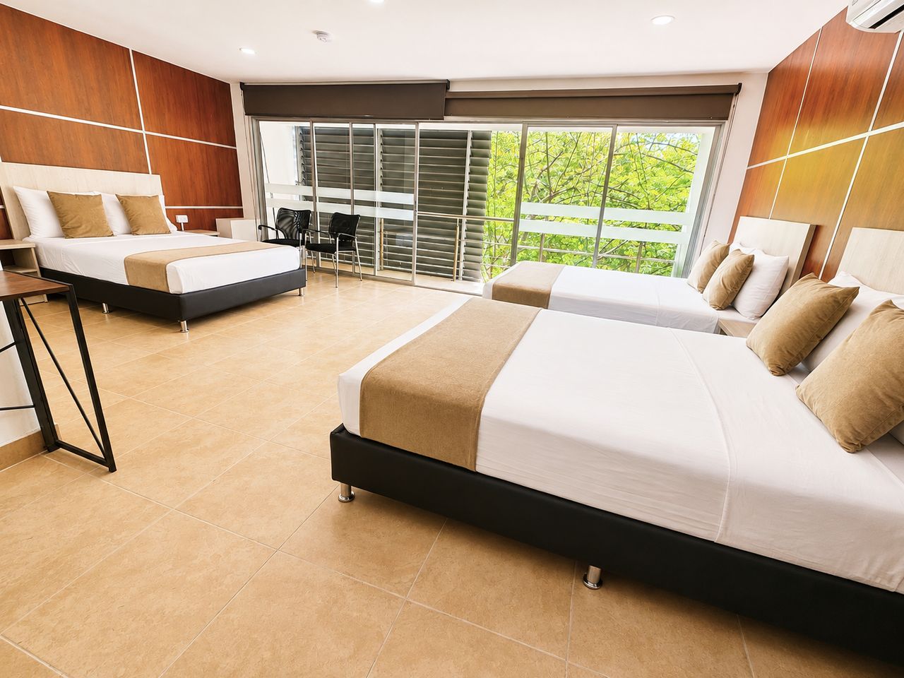 A hotel room with two beds, a dining area, and a view of greenery.