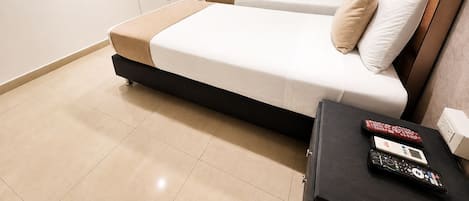 Una habitación de hotel moderna con un televisor de pantalla plana montado en la pared, una cama con cabecero, una mesita de noche con un control remoto, y un baño visible a través de una puerta abierta.