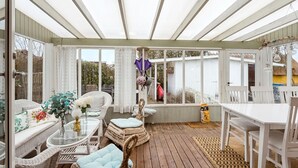 Eine überdachte Terrasse mit Korbmöbeln, einem Glastisch und einem weißen Tisch.