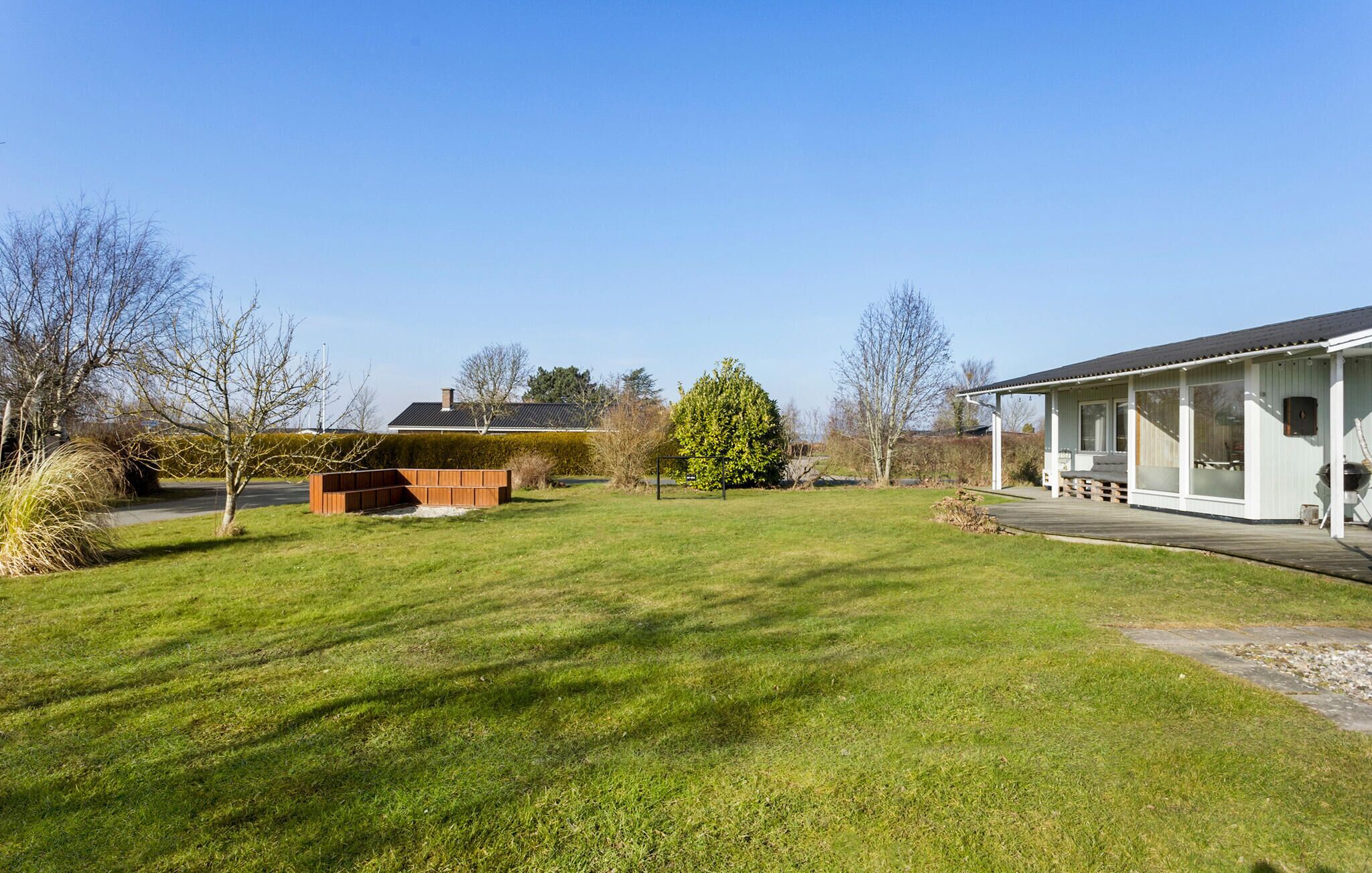 Une pelouse bien entretenue, agrémentée d’une terrasse en bois, d’un espace salon extérieur abrité et d’un grand arbre en arrière-plan.