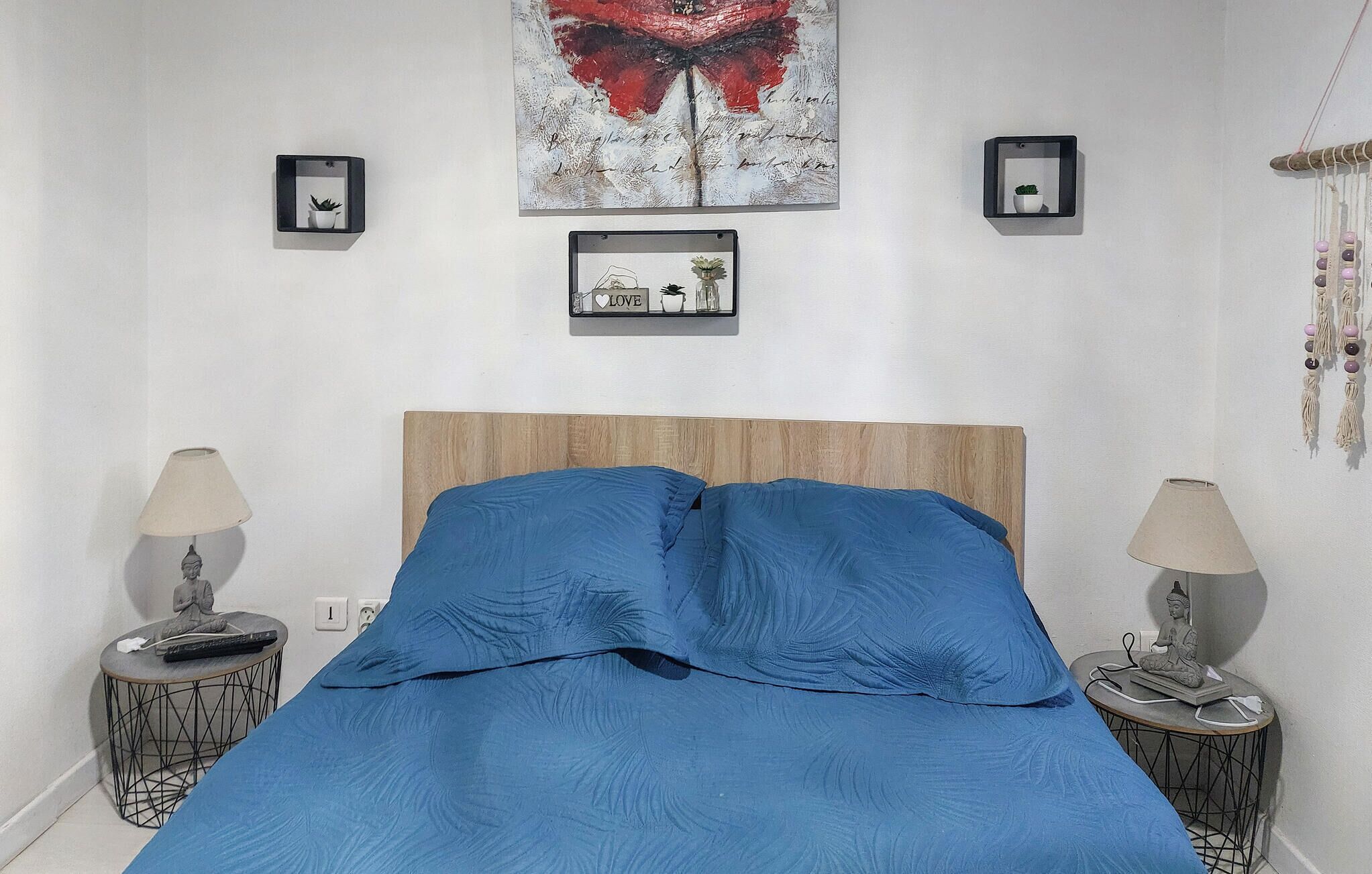 Une chambre à coucher avec une tête de lit en bois, une couvre-lit bleue, deux tables de chevet avec des lampes et des œuvres d’art murales.
