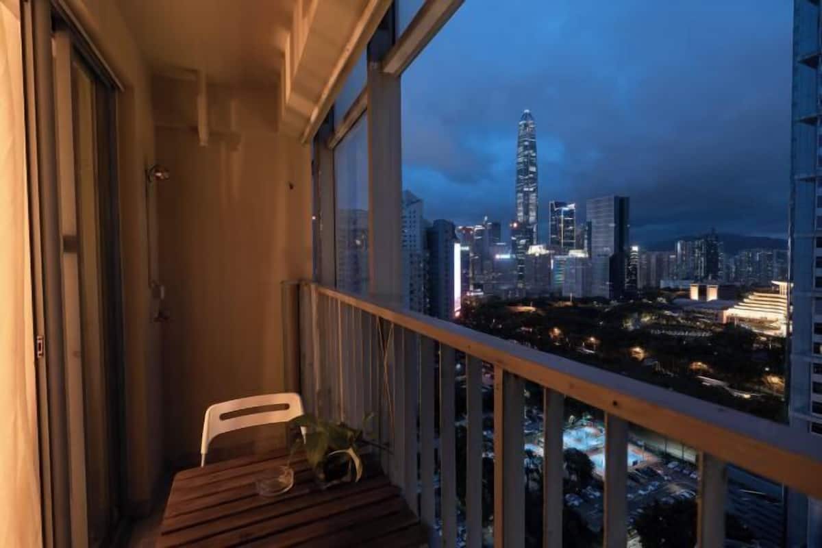 Varanda com mesa e cadeira de madeira, com vista para um horizonte urbano com edifícios iluminados ao anoitecer.