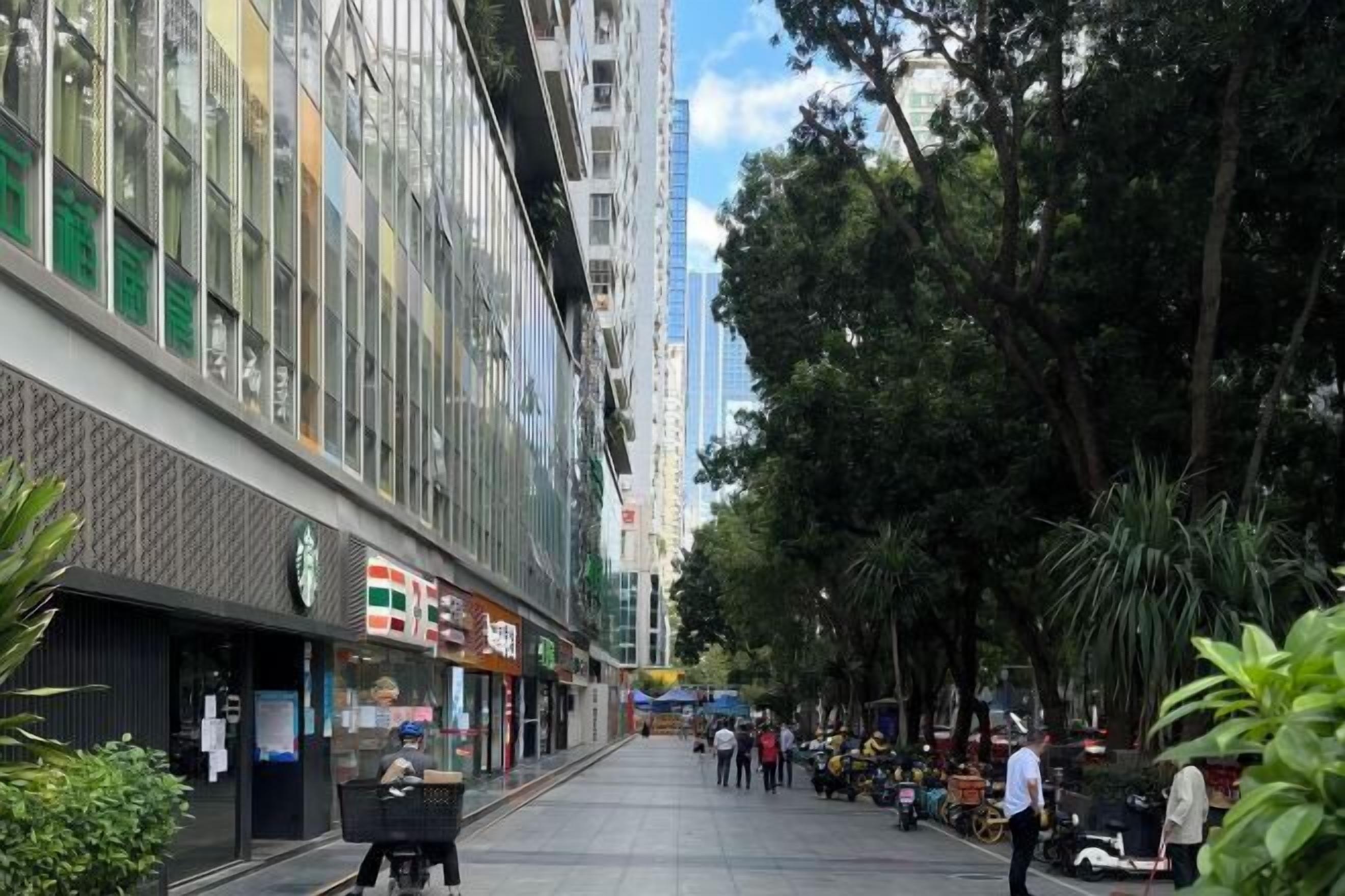 A street lined with modern buildings, a Starbucks, and pedestrians.