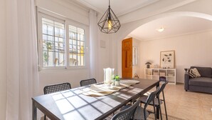 A dining area with a long table, chairs, a hanging light fixture, and a view through large windows. - 2 bedroom stunning home in La Zenia (La Zenia)