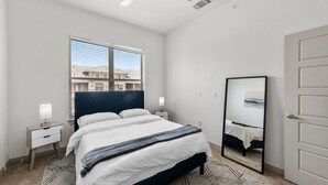 Une chambre à coucher avec un lit, une table de chevet, un miroir et une fenêtre avec des stores.