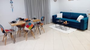 A modern living room with a blue sofa, a dining table with colorful chairs, and a white floor. - Charming 1-bedroom apartment with WiFi, AC in delightful Sarandë (Sarandë)
