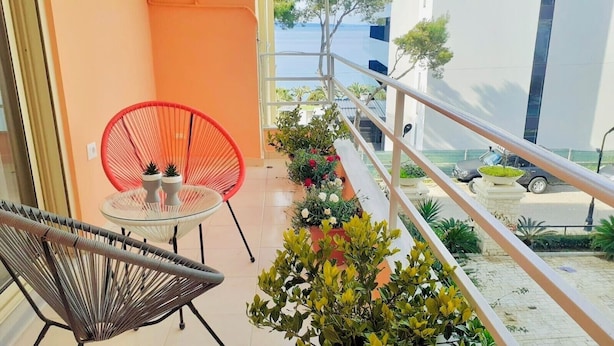 A balcony with a glass table and chairs, potted plants, and a view of the sea and buildings. - Charming 1-bedroom apartment with WiFi, AC in delightful Sarandë (Sarandë)