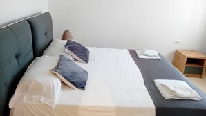 A neatly made bed with white and gray bedding, two pillows, and a wooden nightstand with a lamp. - Charming 1-bedroom apartment with WiFi, AC in delightful Sarandë (Sarandë)