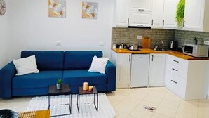 A compact living space with a blue sofa, a small coffee table, and a kitchen area with white cabinets and a microwave. - Charming 1-bedroom apartment with WiFi, AC in delightful Sarandë (Sarandë)