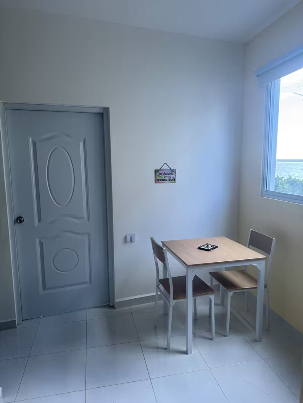 Een kleine kamer met een tafel, twee stoelen, een deur en een raam met uitzicht.