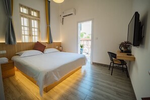 A bedroom with a bed, bedside table, chair, and a TV mounted on the wall.