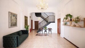 Un hall d’entrée spacieux avec un grand escalier, un canapé vert et des plantes décoratives.