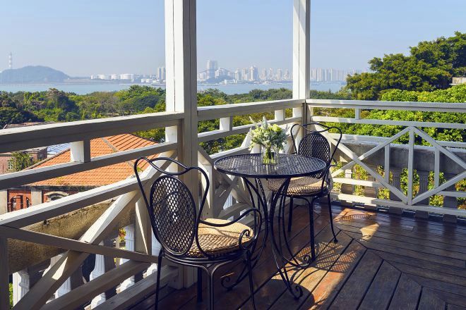 A balcony with a table and chairs, overlooking a cityscape and greenery.