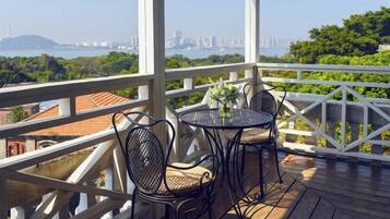 A balcony with a table and chairs, overlooking a cityscape and greenery.