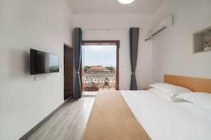 A hotel room with a bed, a TV, an air conditioner, and a view of the outside.