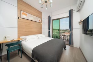 A modern hotel room with a bed, a desk, and a chair. There is a large window with curtains, and a view of the outside.