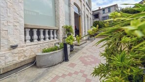 Un bâtiment à la façade en pierre, doté de grandes fenêtres et d’un chemin bordé de plantes en pot.