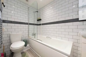Ein Badezimmer mit weiß gefliesten Wänden, einer weißen Badewanne und einer Toilette.