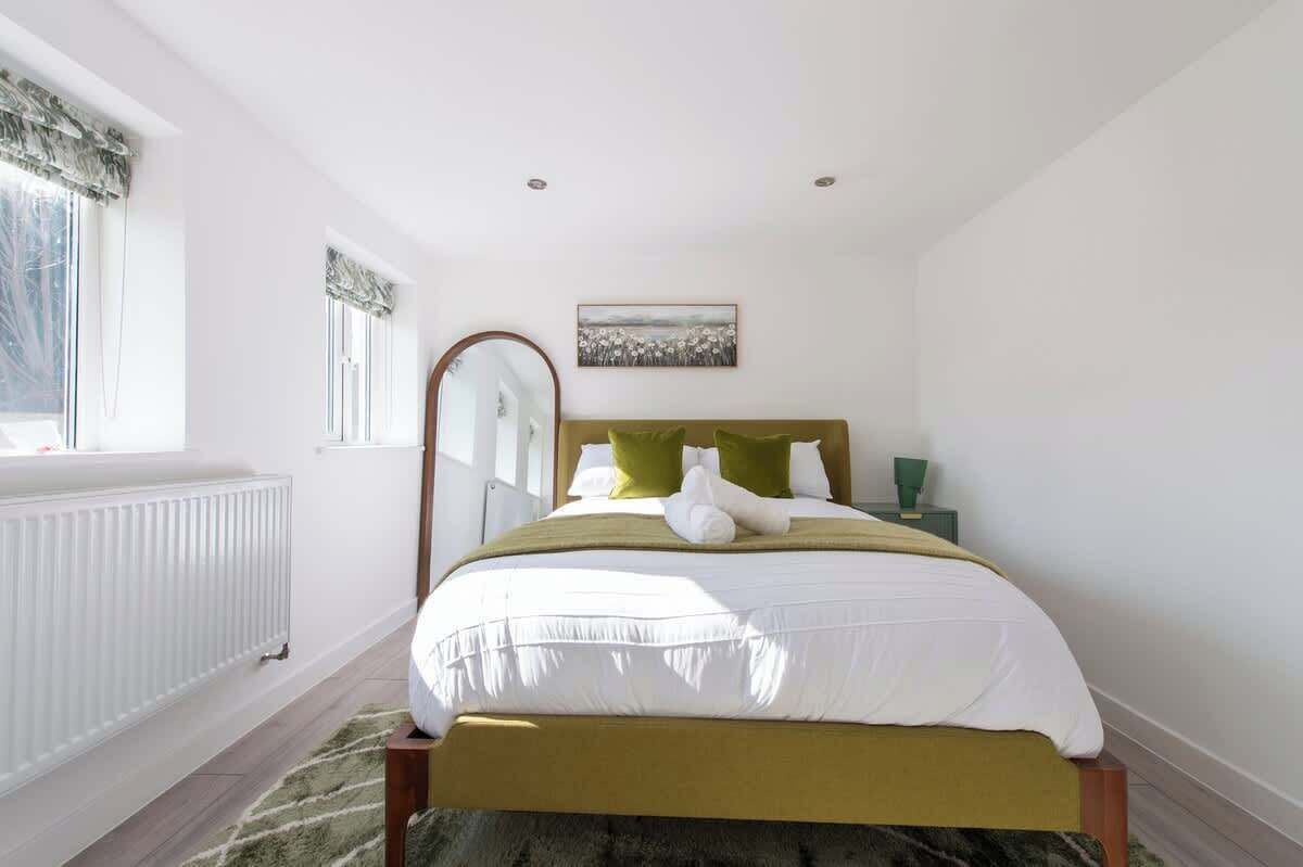 A bedroom with a bed, a radiator, a window with curtains, a mirror, and a painting on the wall.