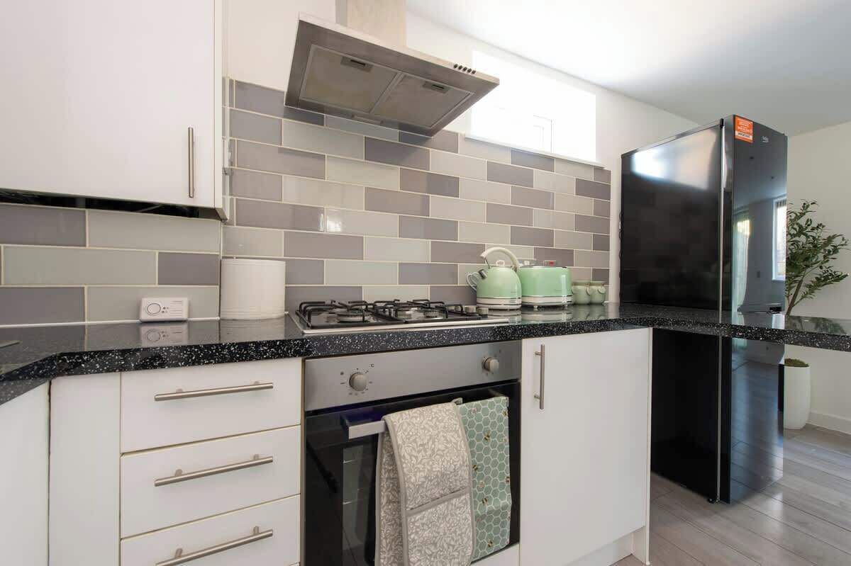 Una cocina moderna con gabinetes blancos, un refrigerador negro, una estufa a gas y un rebozado de azulejos.