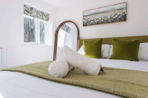 Hotellihuone, jossa on sänky, vihreät ja valkoiset tyynyt, vihreä heittopeitto, kukkakuva ja ikkuna, josta avautuu näkymä puihin.