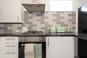 A kitchen with a gas stove, a range hood, a microwave, and a kettle. - The Green Haven-Cozy luxury flat in Crayford (Greater London)