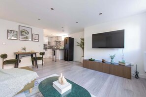 Ein modernes Wohnzimmer mit Flachbildfernseher, Essbereich und einer Küche im Hintergrund.