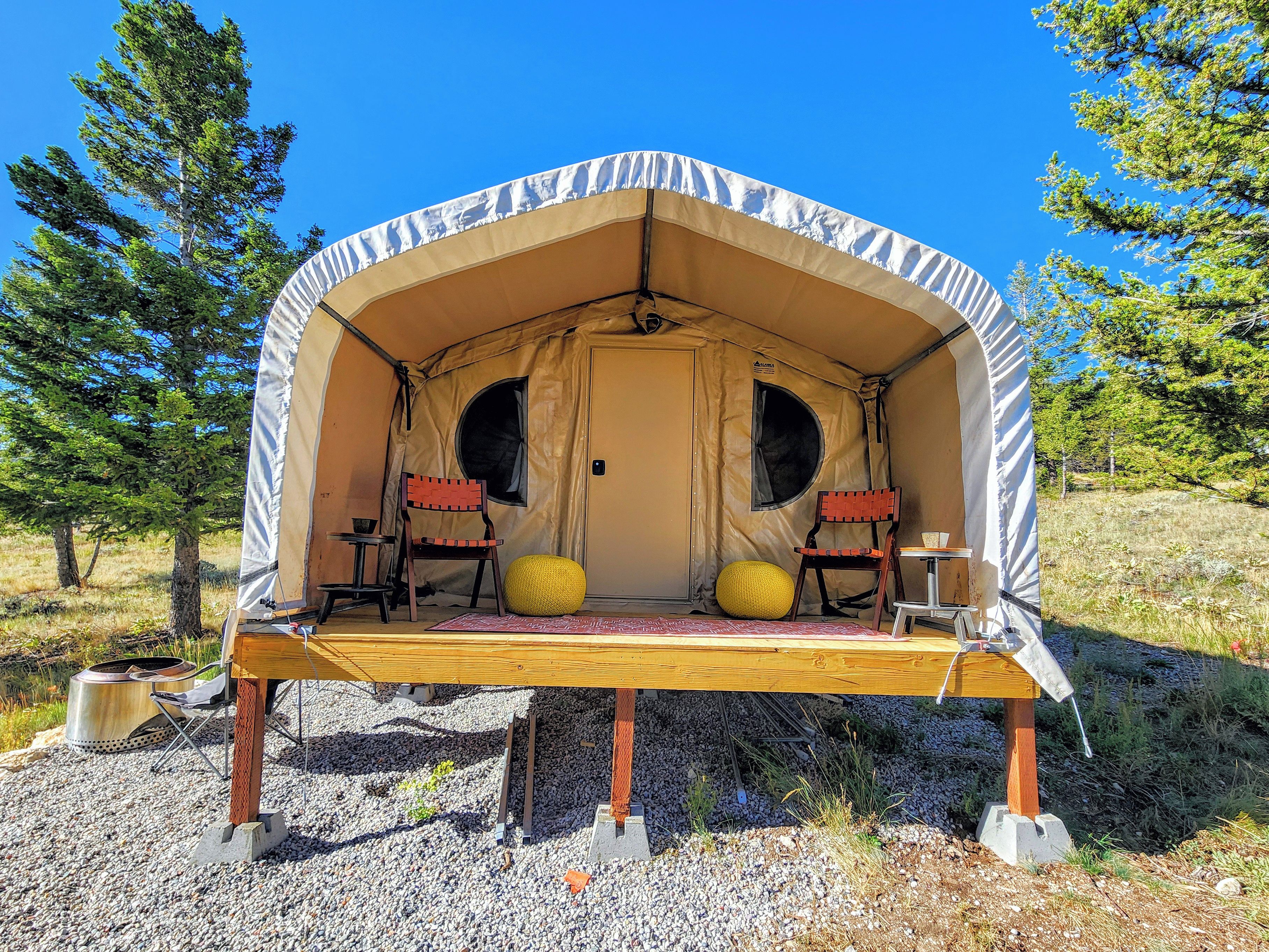 A tent with two chairs and a table, set on a gravel surface with trees in the background.