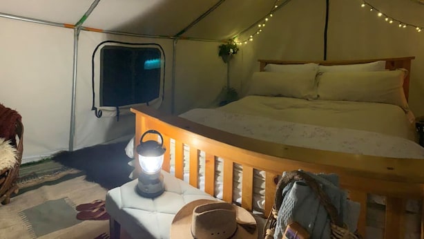 Ein Zelt mit Bett, einer Laterne und einem kleinen Tisch mit Hut und Badeschlappen.