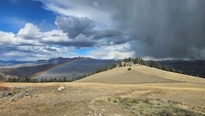 Eine hügelige Landschaft mit Regenbogen, Zaun und blauem Himmel.